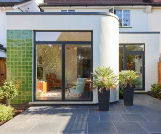 exterior of house with curved white extension with flat roof, black framed patio doors and green tiled section to left hand side of garden facing doors