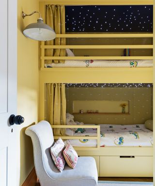 A yellow bunk bed with fairy lights in the canopies