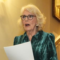 Queen Camilla wearing a green dress reading from a paper 