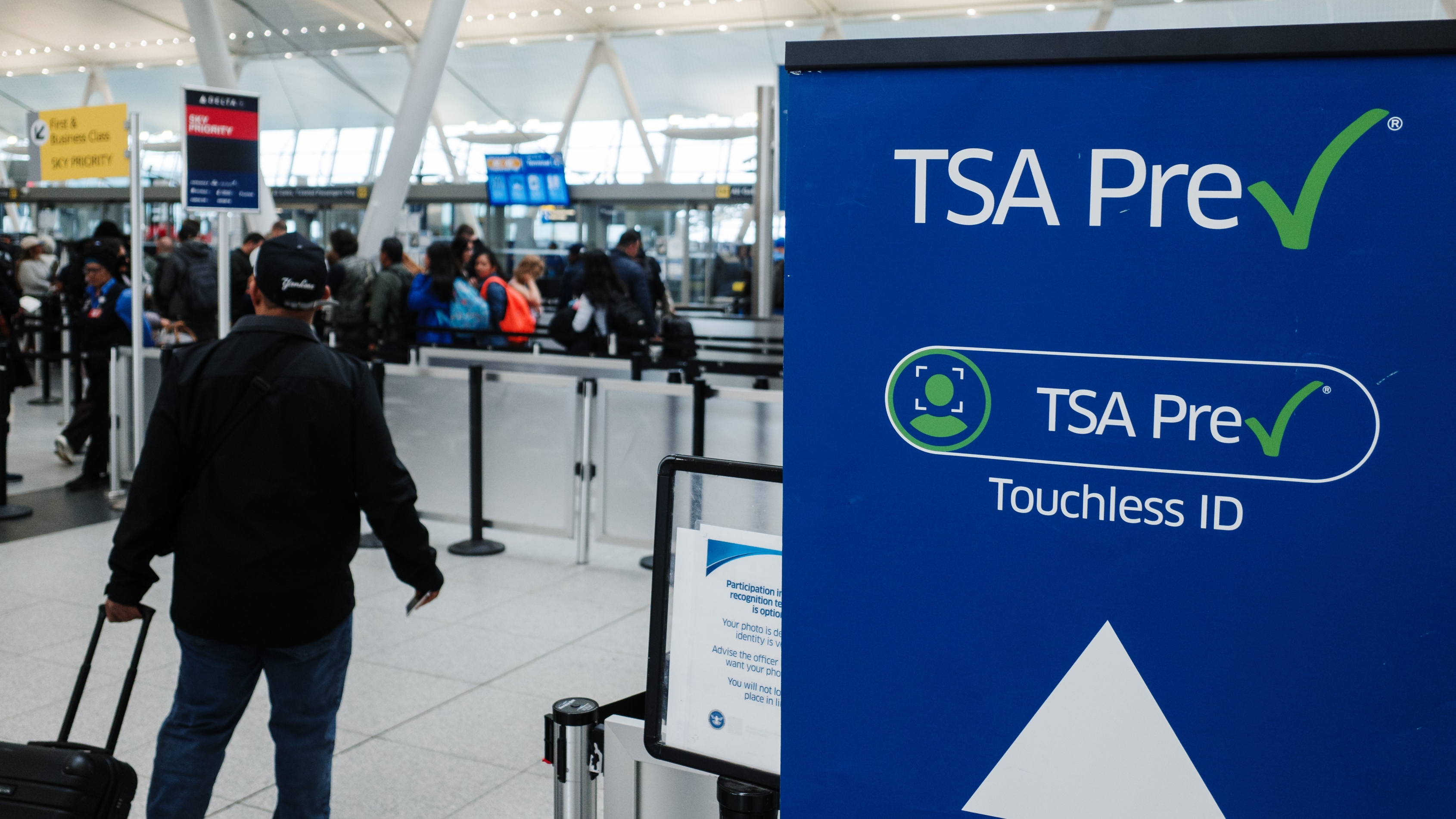 A traveler with a rolling suitcase walks toward the TSA PreCheck Touchless ID lane.