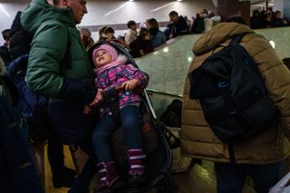 A child is carried down the steps in her stroller. Hundreds of people seek shelter underground, on the platform, inside the dark train cars, and even in the emergency exits, in metro subway station as the Russian invasion of Ukraine continues, in Kharkiv, Ukraine, Thursday, Feb. 24, 2022.