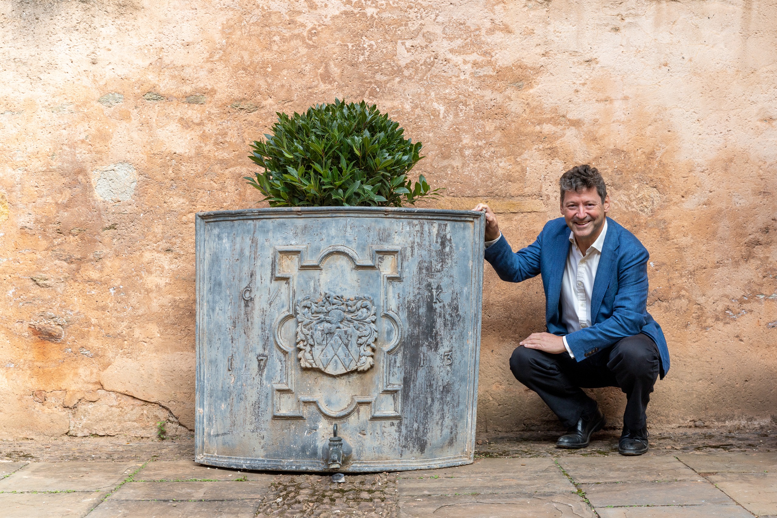 A man in dark trousers and a blue blazer squatting next to a cistern