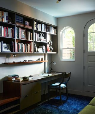 small home office with a small green sleeper sofa and mid century office shelves