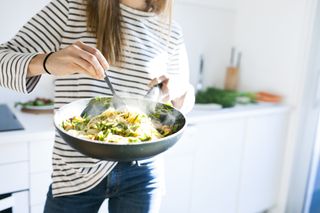 Benefits of eating organic: Young woman holding pan with vegan pasta dish