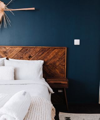 bedroom with dark blue wall, wooden bed and small white thermostat on wall