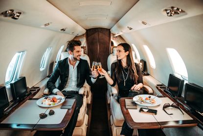 A rich couple raises champagne flutes on a private plane.