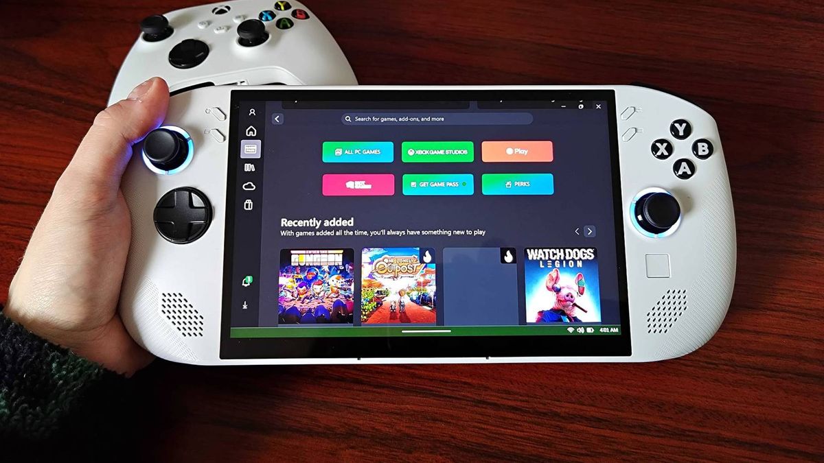 Hand holding Lenovo Legion Go S in white with woodgrain desk and Xbox controller in backdrop.