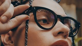 Woman pressing the action button on a pair of black Ray-Ban Meta smart glasses.