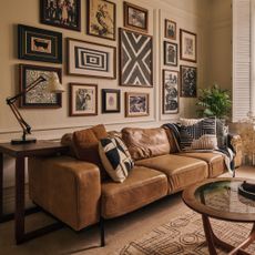 A living room with a three-seater brown leather sofa on narrow black metal legs and a gallery wall above it