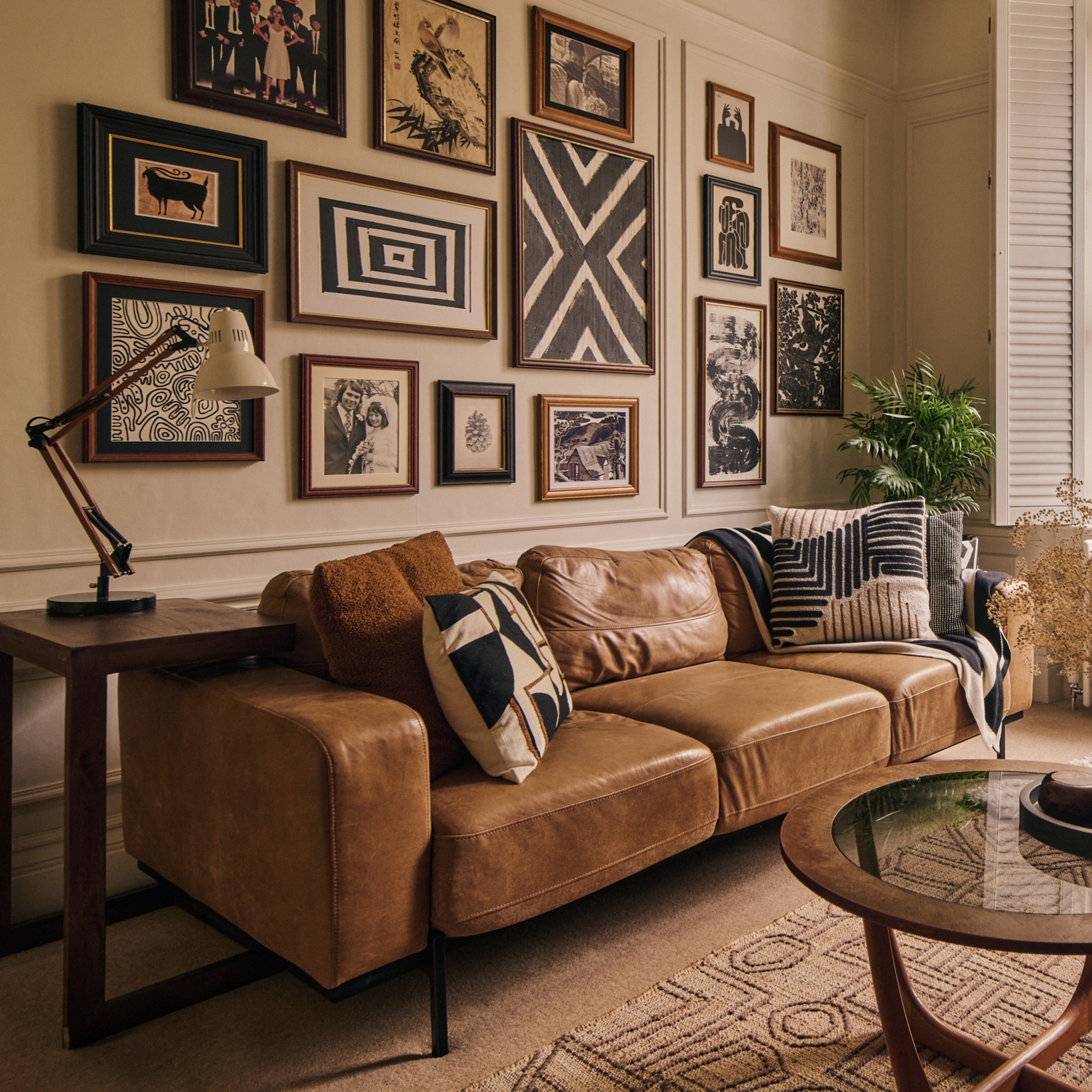 A living room with a three-seater brown leather sofa on narrow black metal legs and a gallery wall above it