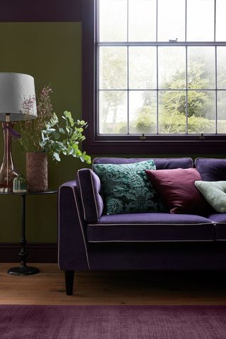 purple sofa under window with green walls