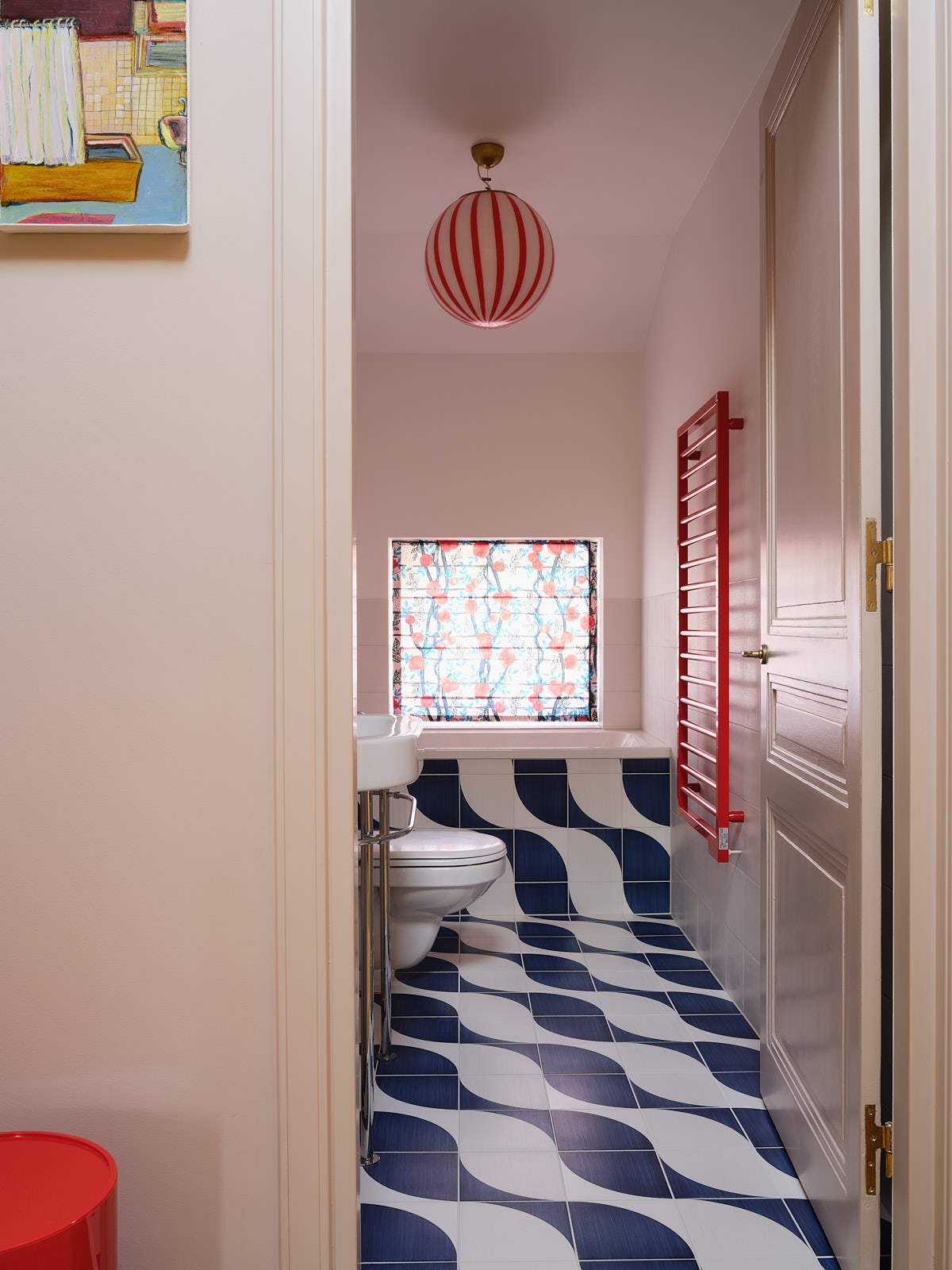 colorful bathroom with pink walls, wave patterned tiles, red towel rack, red and pink light fitting, and patterned window shades