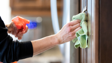 A person using a microfiber cloth and a cleaning spray to wipe kitchen cabinets.