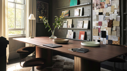 A decorated home office with a wall of floating green ledges, a wood desk, a board of fabric swatches, and a large push window