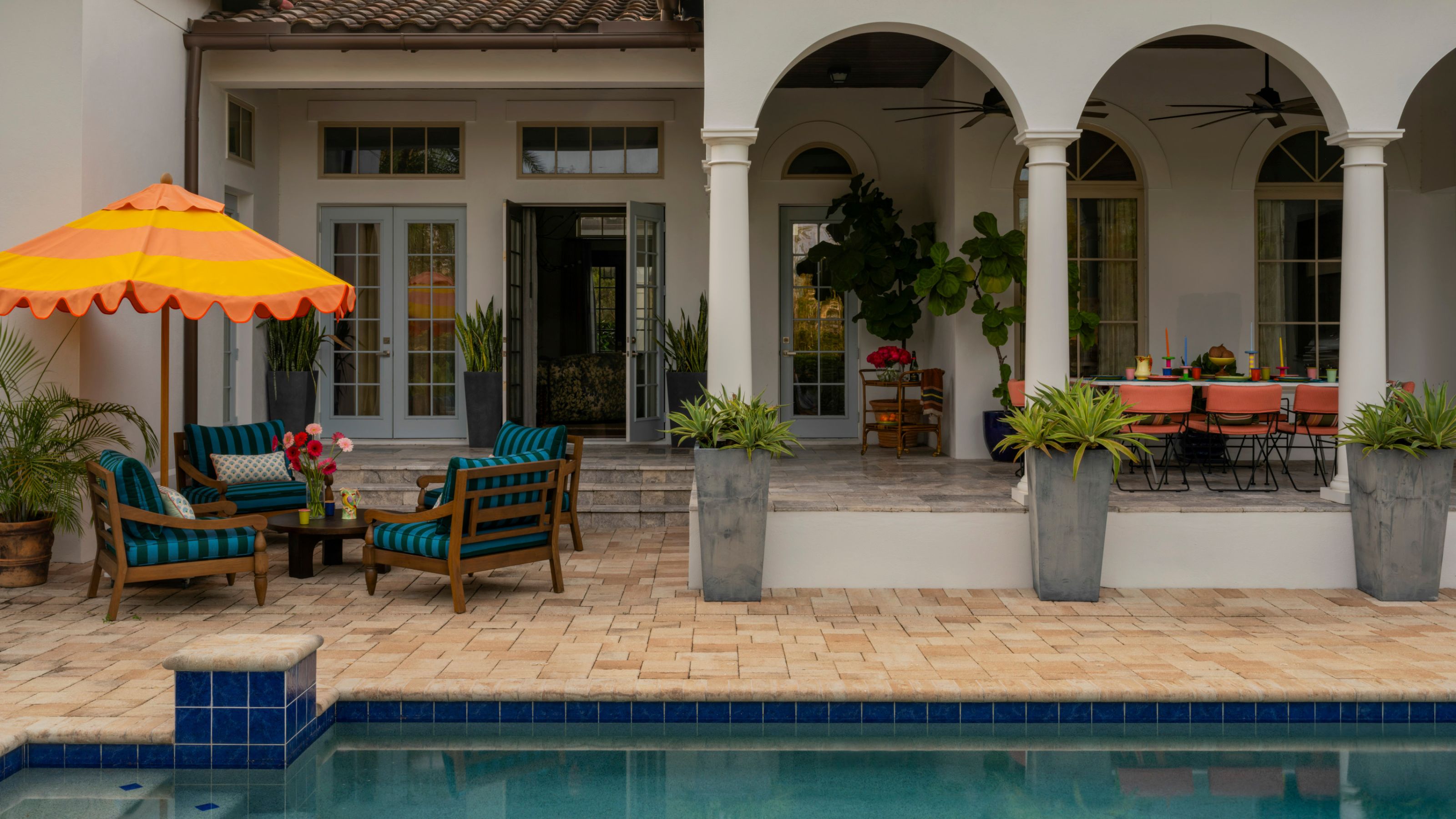 a florida pool area with arched covered porch and colorful striped furniture and umbrella