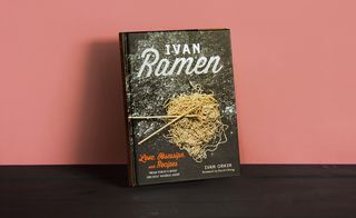 Front cover of the book 'Ivan Ramen: Love, Obsession, Recipes', Black background, white and red lettering, noodles, flour and chopsticks image, dark wood surface, orange background
