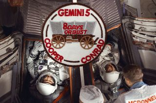 Astronauts Gordon Cooper (left) and Charles Conrad are seen in the Gemini 5 spacecraft just before launching on their "8 Days or Bust" mission in 1965. The crew was the first to design and wear a mission patch, as shown. 