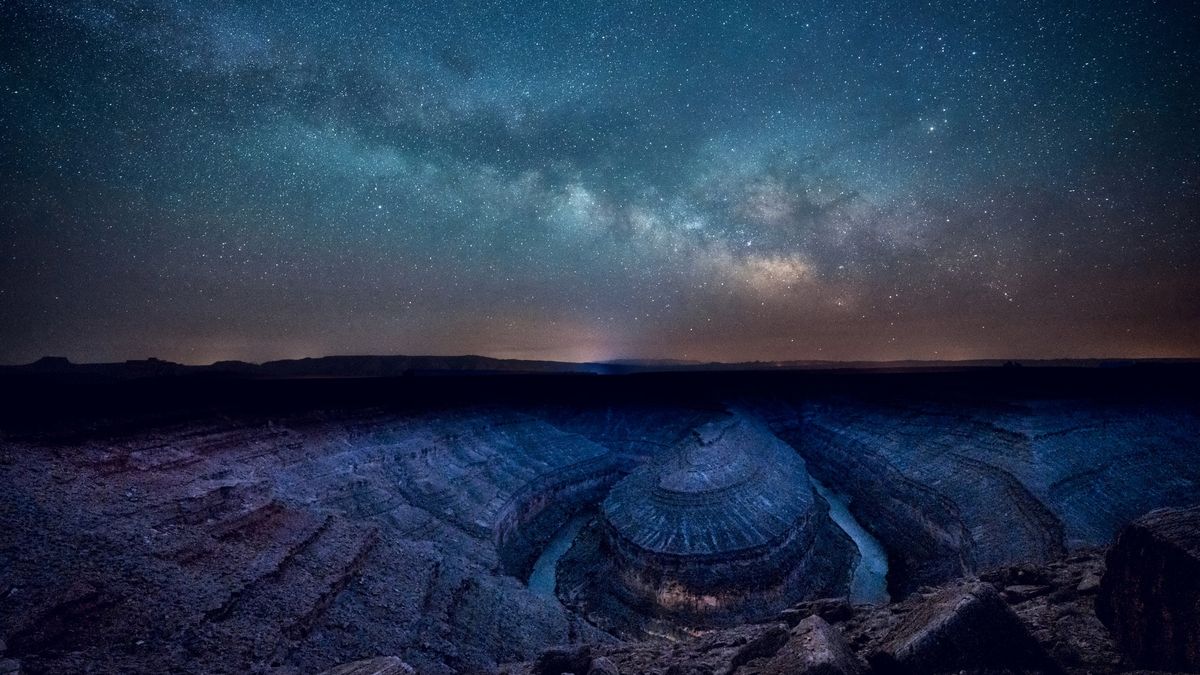 The milky way stretches across the starry sky above a meandering river below. 