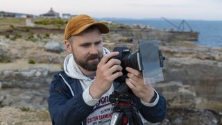 A photographer using a camera with a square filter holder attached and a large ND grad on the front of it