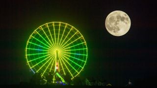 brightly lit green and yellow ferris wheel with a large full moon to the right