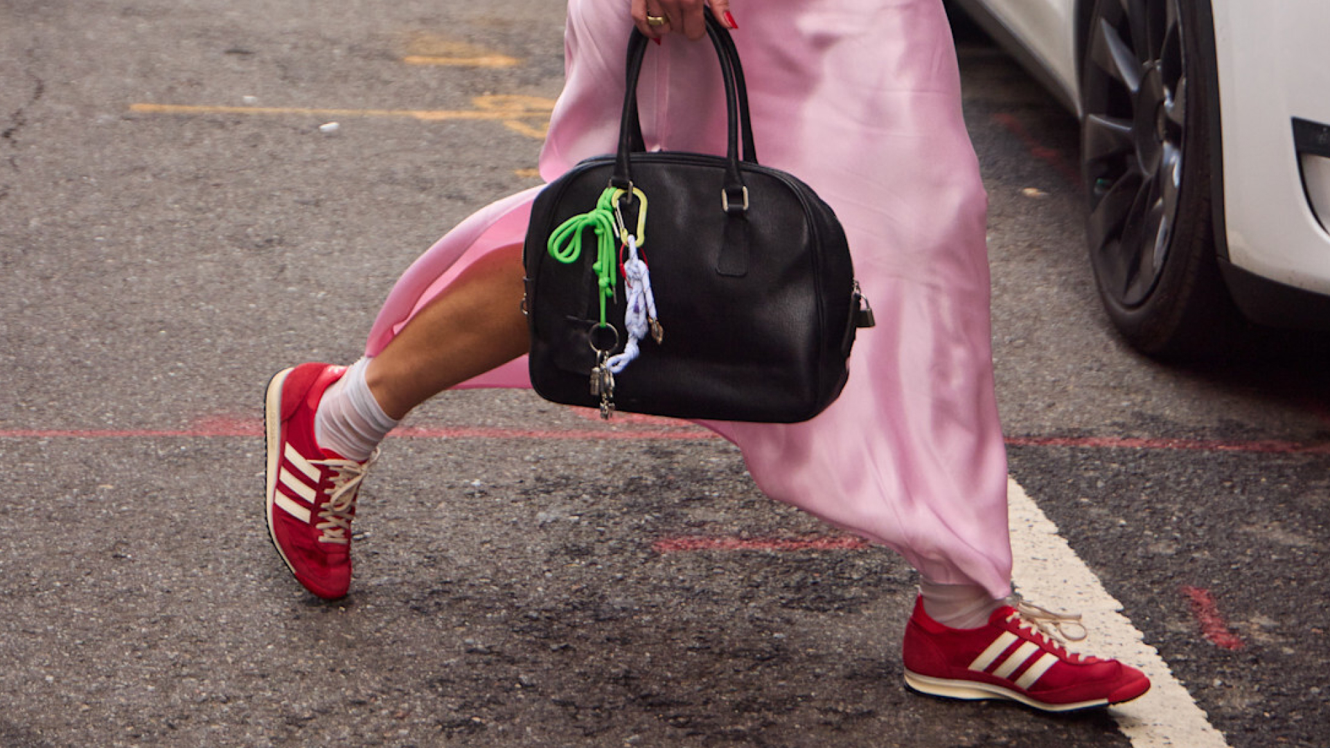 a woman wearing a pink silk dress wearing red sneakers carring a black handbag