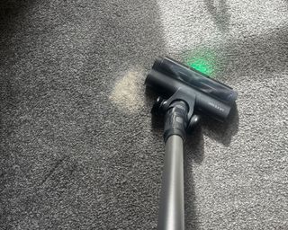 Ultenic U12 Vesla cordless vacuum cleaner being used on oatmeal on gray carpet. Even with sunshine pouring into the room, the green LED light is visible on ground