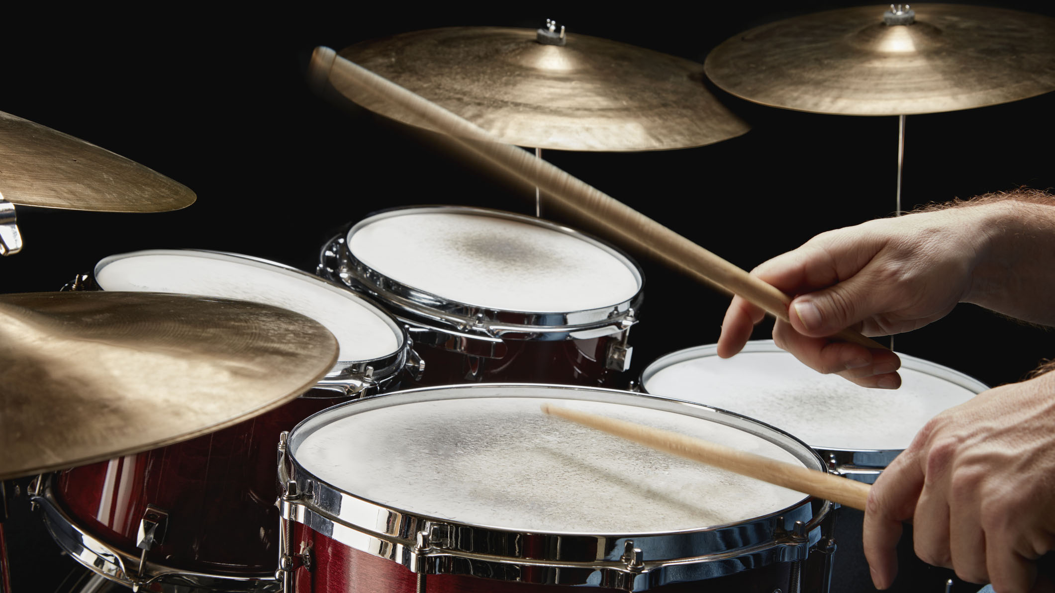 Drummer holding drumsticks and playing a red drum set
