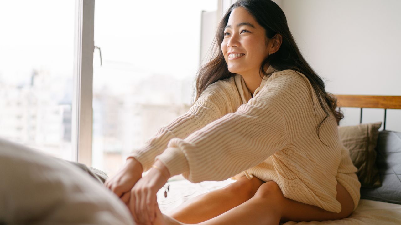 A woman stretches over her legs and holds her feet in her bed in the morning