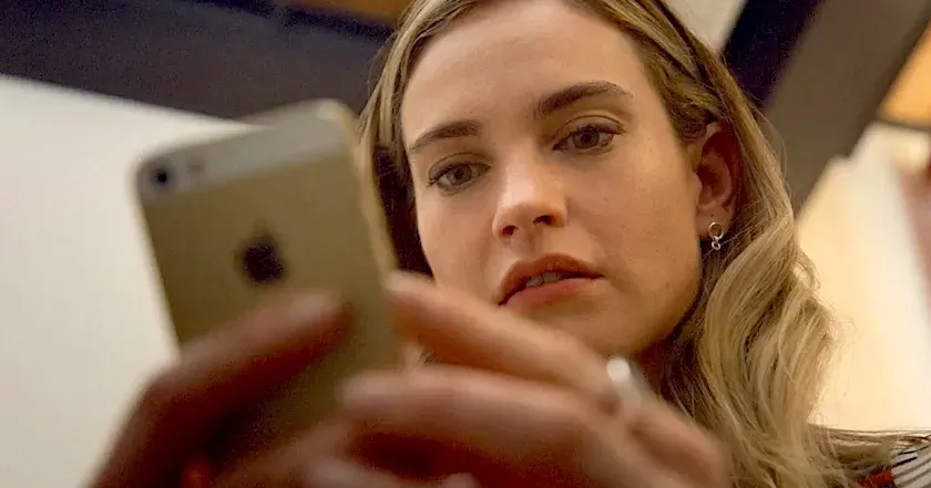 Lily James as Whitney Wolfe Heard, looking at her cellphone.