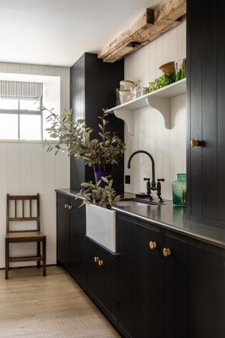 A wooden chair with a large sink and dark cupboards featuring vertical lines