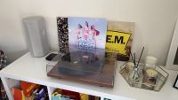 The walnut-finished Pro-Ject T1 turntable, photographed on a white bookcase with an assortment of records behind it