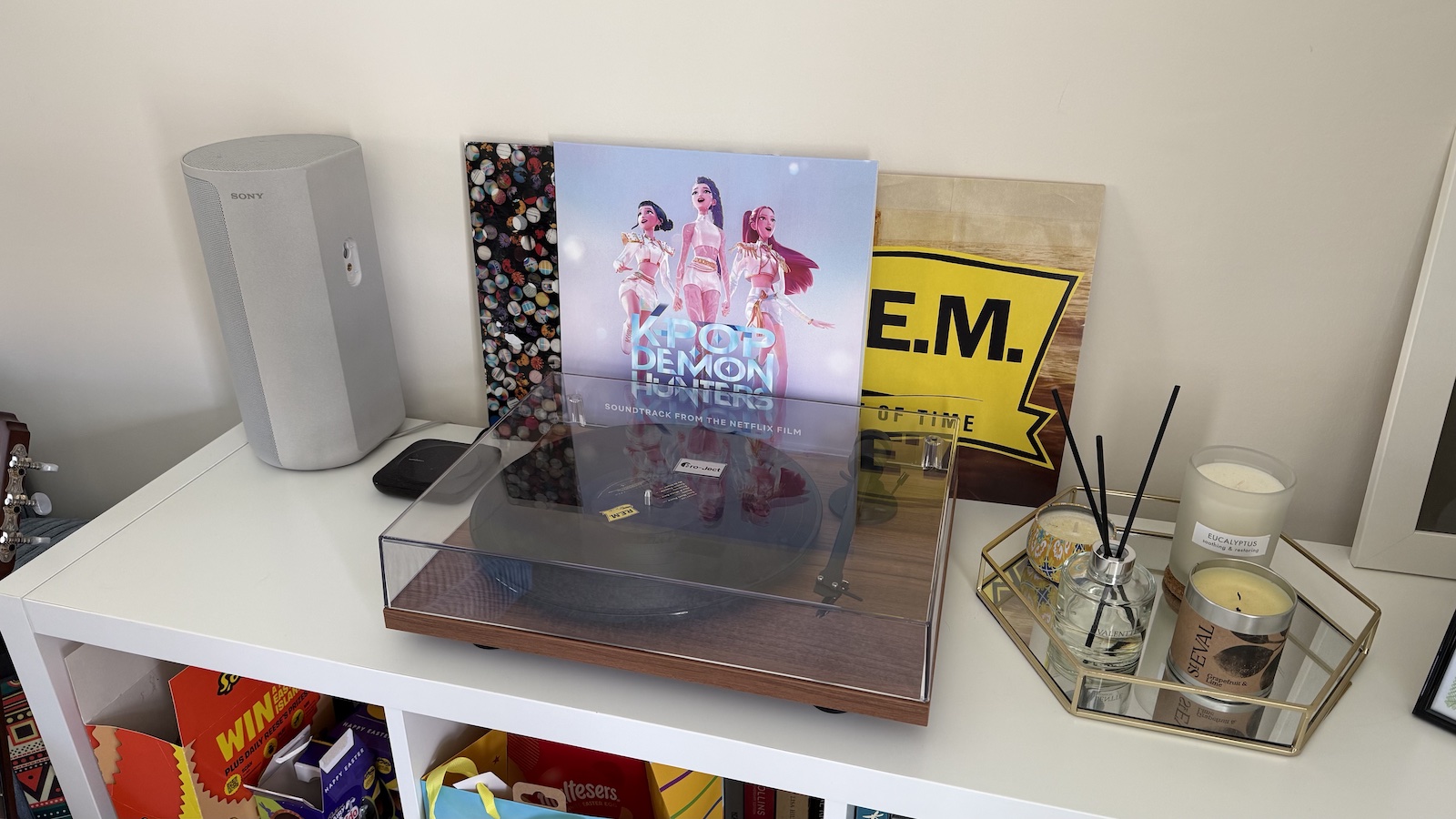 The walnut-finished Pro-Ject T1 turntable, photographed on a white bookcase with an assortment of records behind it
