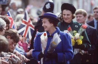 The Queen receiving flowers from the public with the Duchess of Grafton standing behind her.