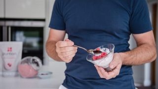 Person eating a yoghurt snack with berries in the kitchen