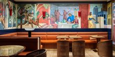 A clad-in-murals-wood-and-leather hotel bar showcases a figurative wall-large painting in earthy tones, along with 1970s-inspired sculptural furniture.