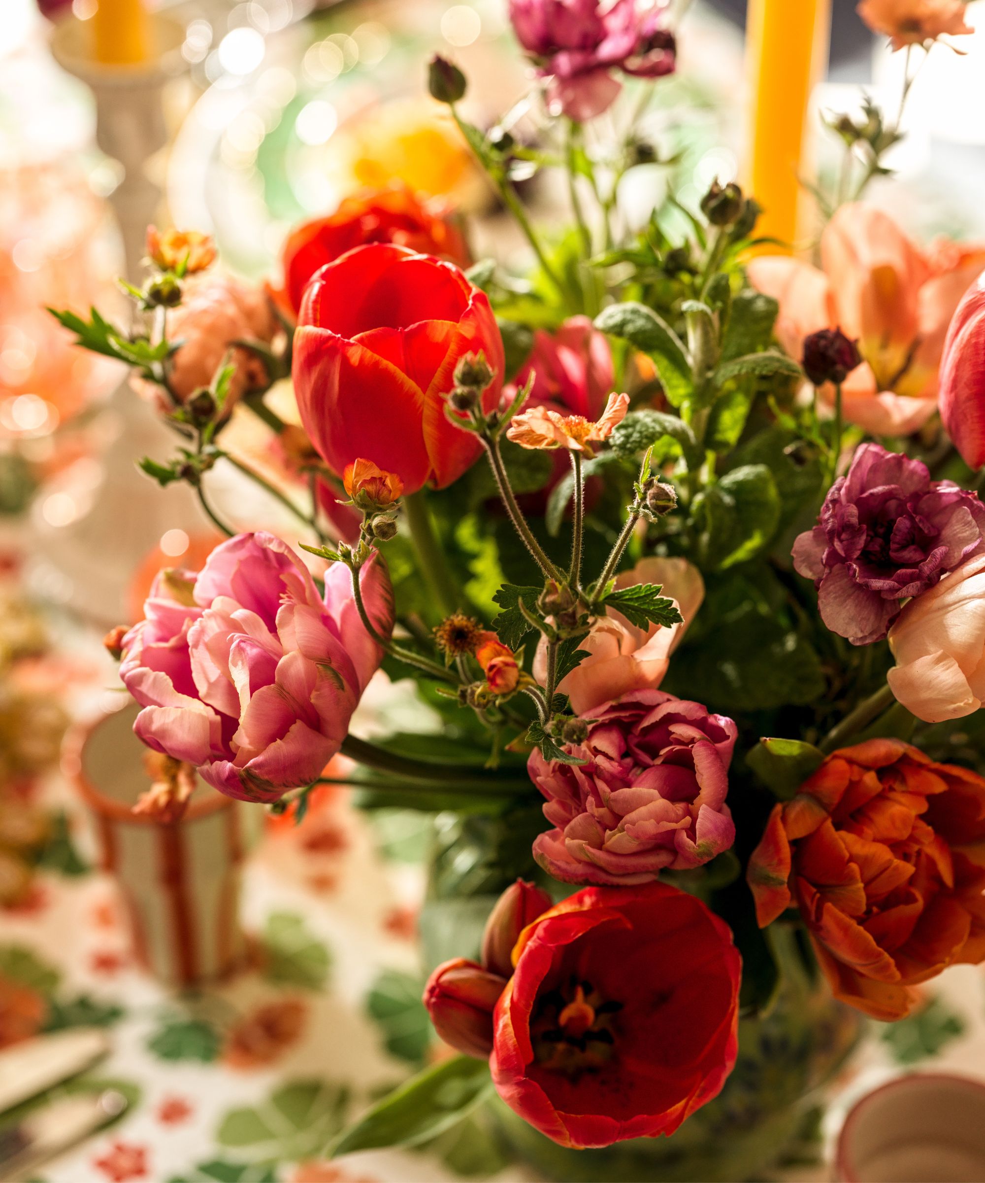A close-up shot of a lush floral arrangement featuring bright red and pink ruffled tulips mixed with delicate orange wildflowers