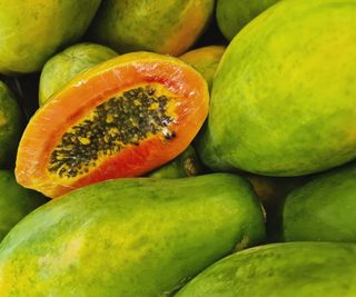 A cut open papaya to reveal the black seeds inside, plus other whole ripe fruits