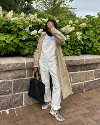 Yusra Siddiqui wearing overalls and Vans checkered sneakers and beige trench coat