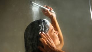 Woman seen washing her hair with shampoo and a silver showerhead