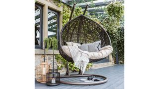 Barker and Stonehouse Willow Hanging Garden Chair in a covered garden with a brick wall and lanterns