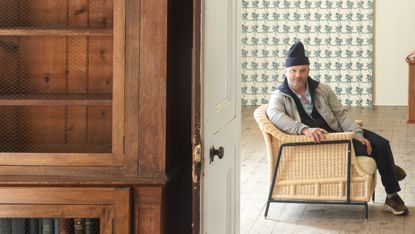 Billy Cotton sat in a chair with wallpaper behind him
