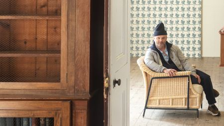 Billy Cotton sat in a chair with wallpaper behind him