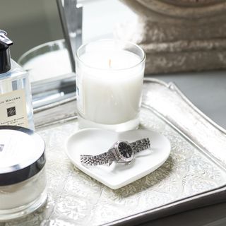 A vanity with a scented candle and a trinket dish with a watch