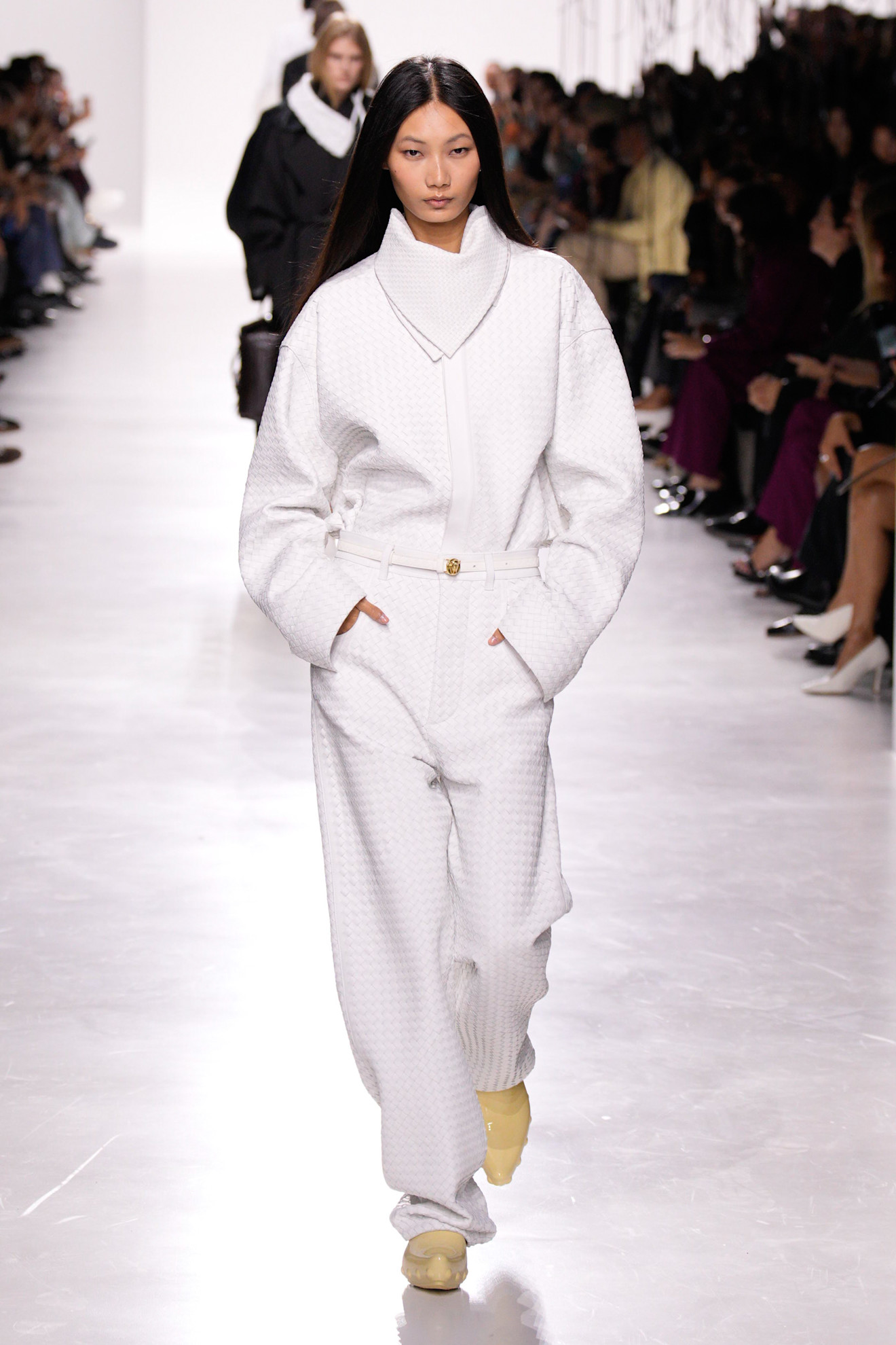 A model walking in the S/S 26 Bottega Veneta show wearing an all-white Intrecciato shirt-and-pant set.