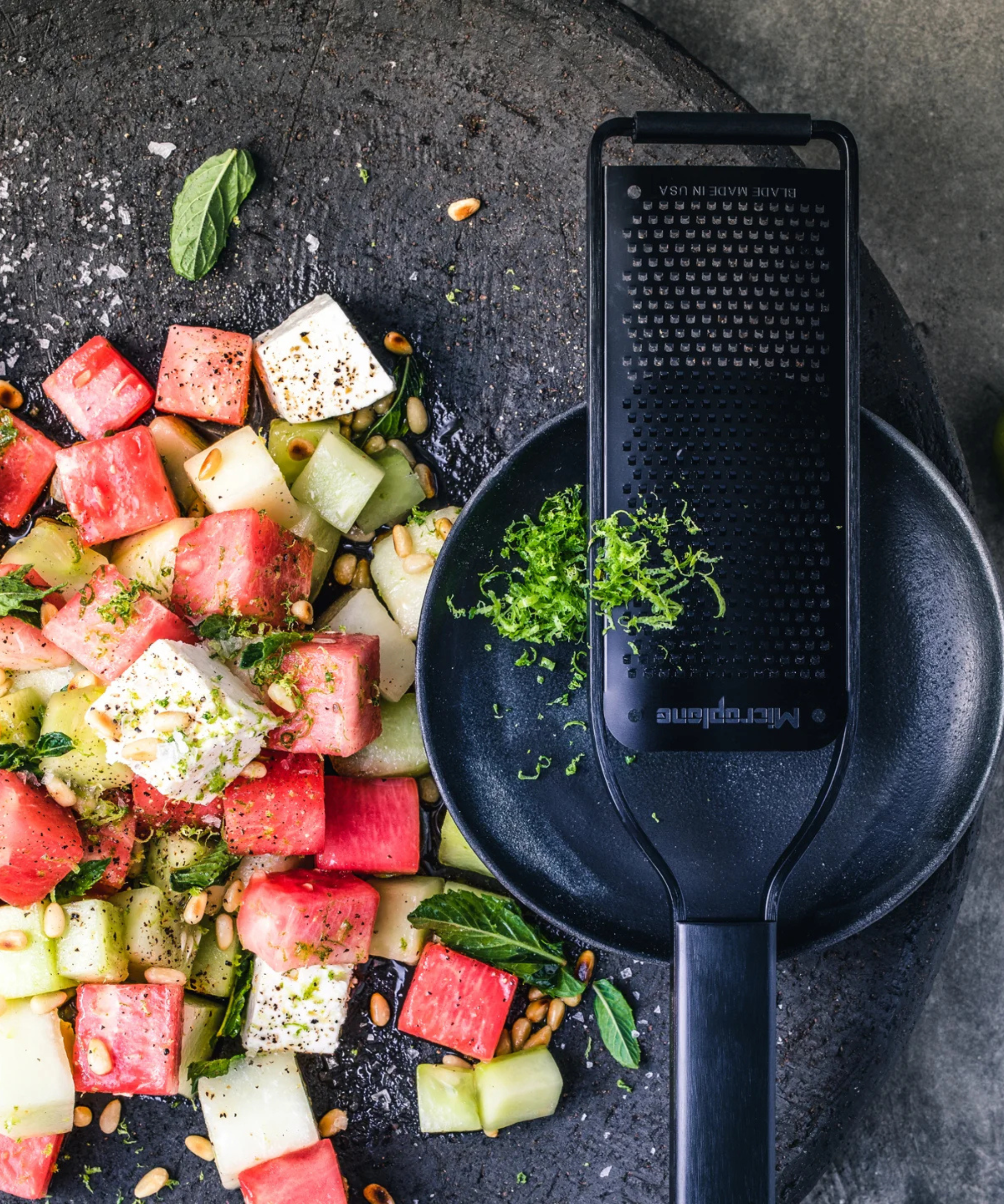 A black microplane zesting fresh herbs for a watermelon and feta salad