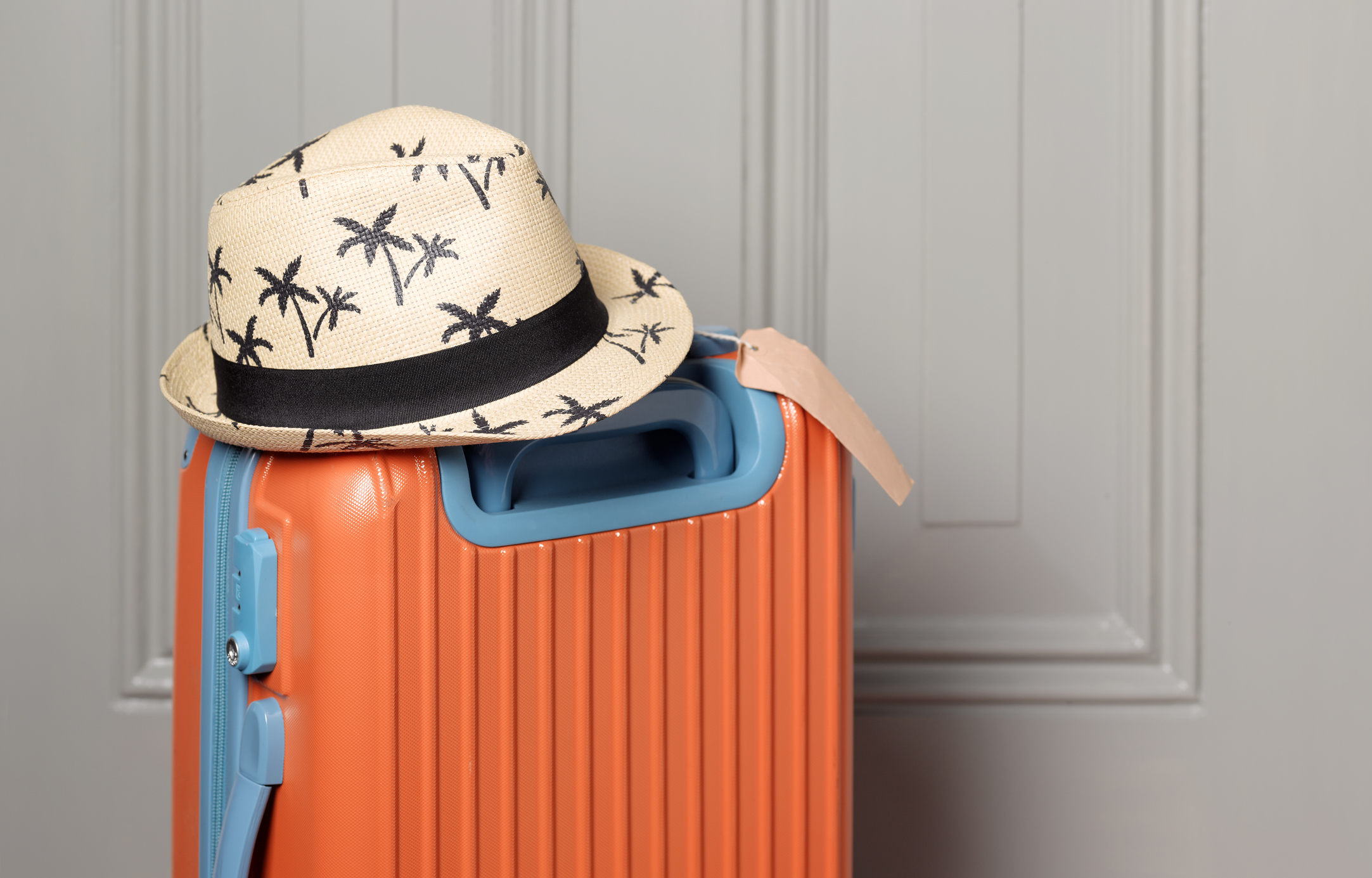 orange suitcase with a Panama hat against a gray door