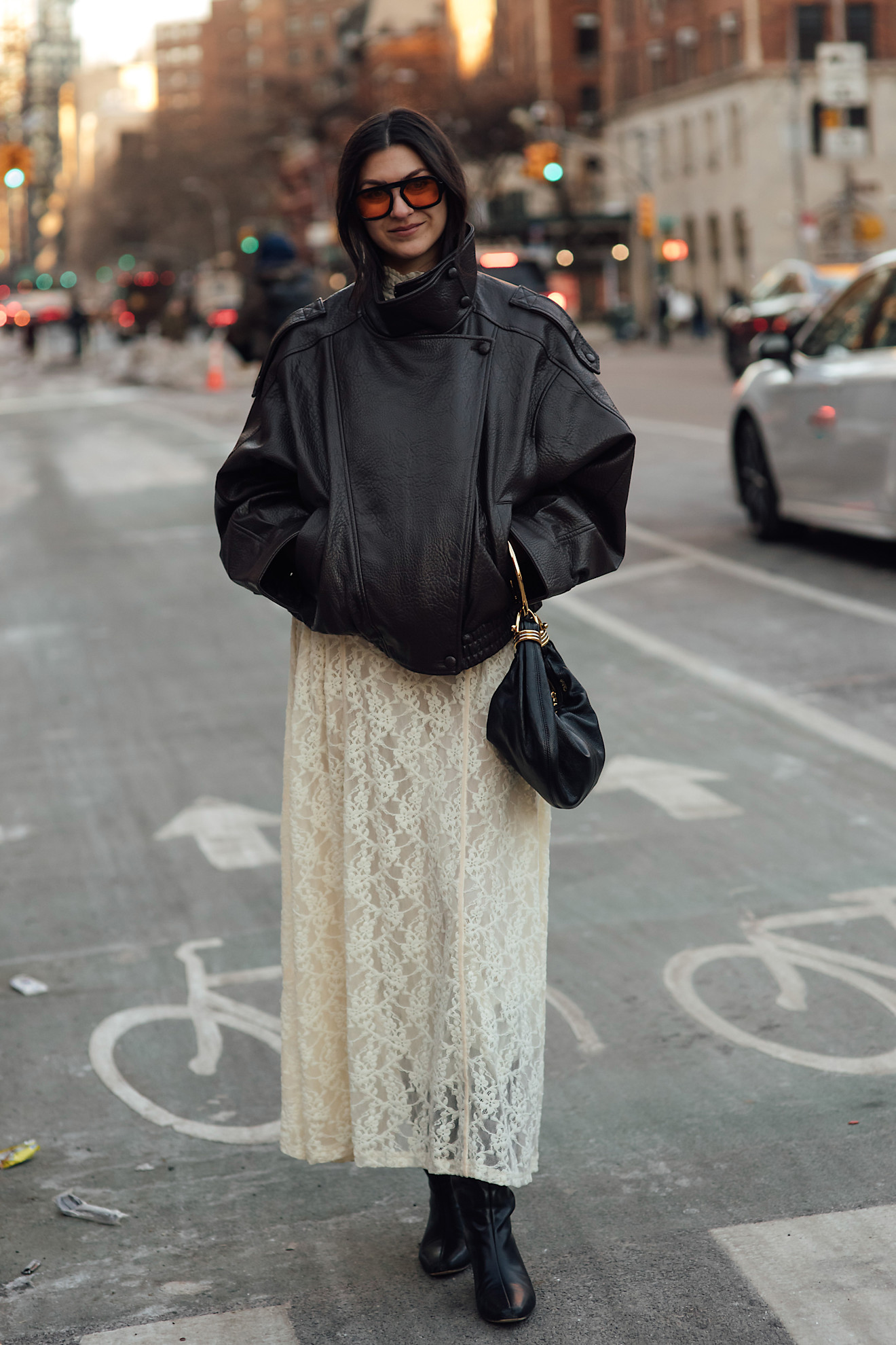 woman wearing leather jacket, white lace skirt, drawstring bag, and boots
