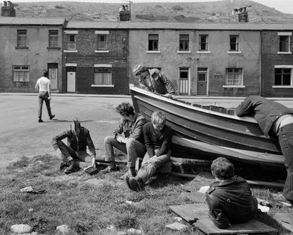 Black & white photo of men working on boat and old building in background