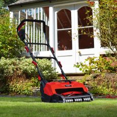 Red lawn mower on grass behind house