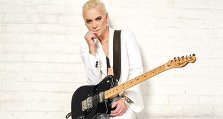 Carmen Vandenberg leans against a white wall with a black Telecaster